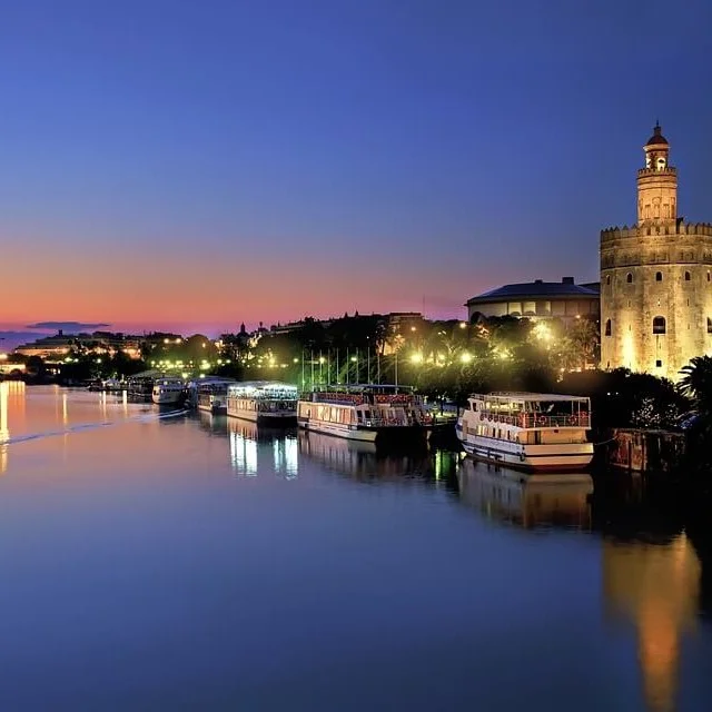 Boats on the Guadalquivir River at night with the Gold Tower in the background